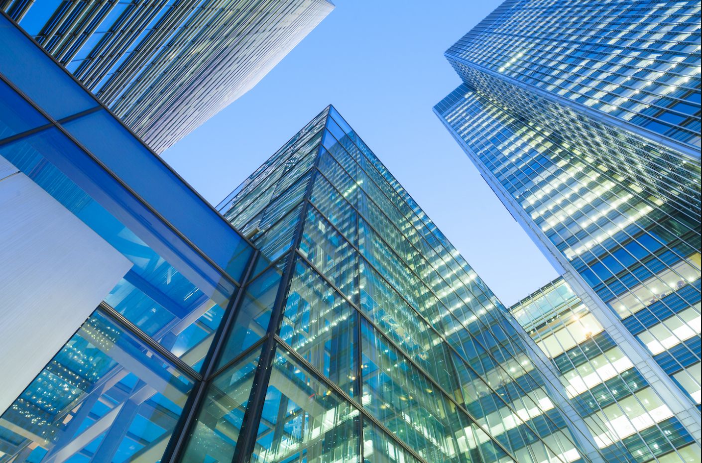 Looking up at tall, clear buildings in a city from below