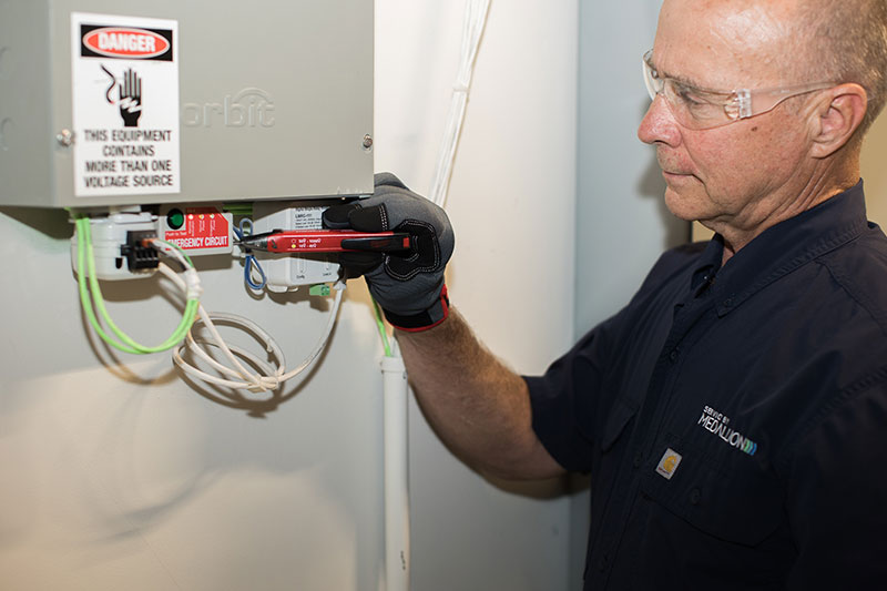 Maintenance technician using electrical testing equipment to inspect an electrical control panel