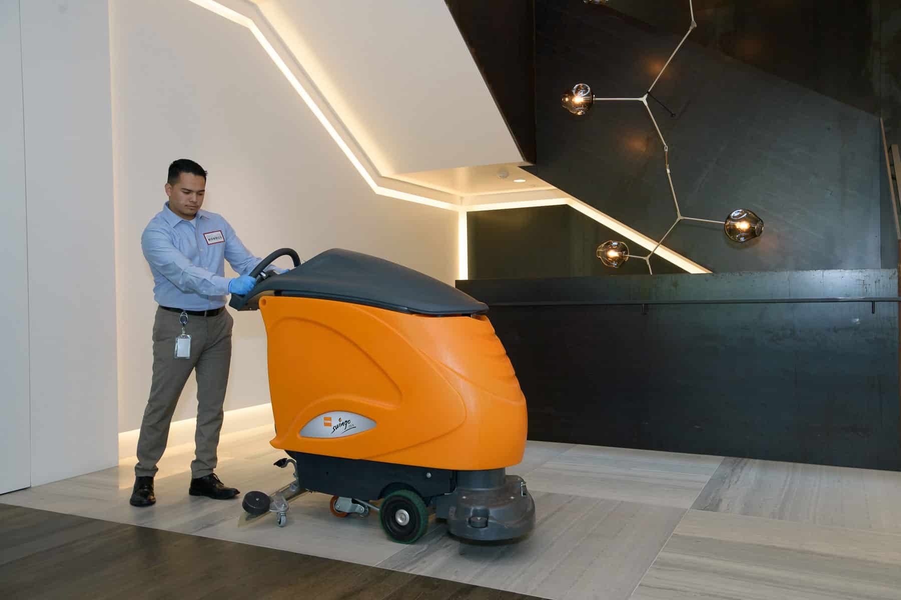 Day porter operating a larger floor scrubber in a modern office