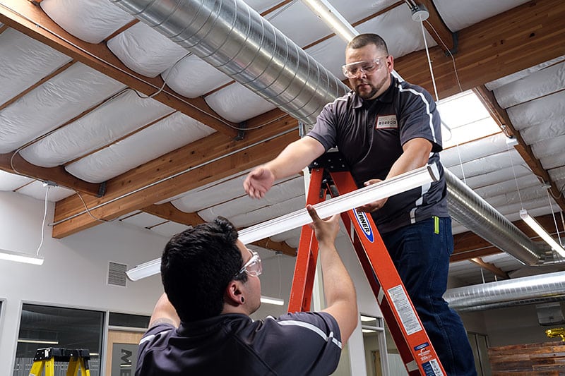 Facility services technicians replacing a lightbulb in a warehouse