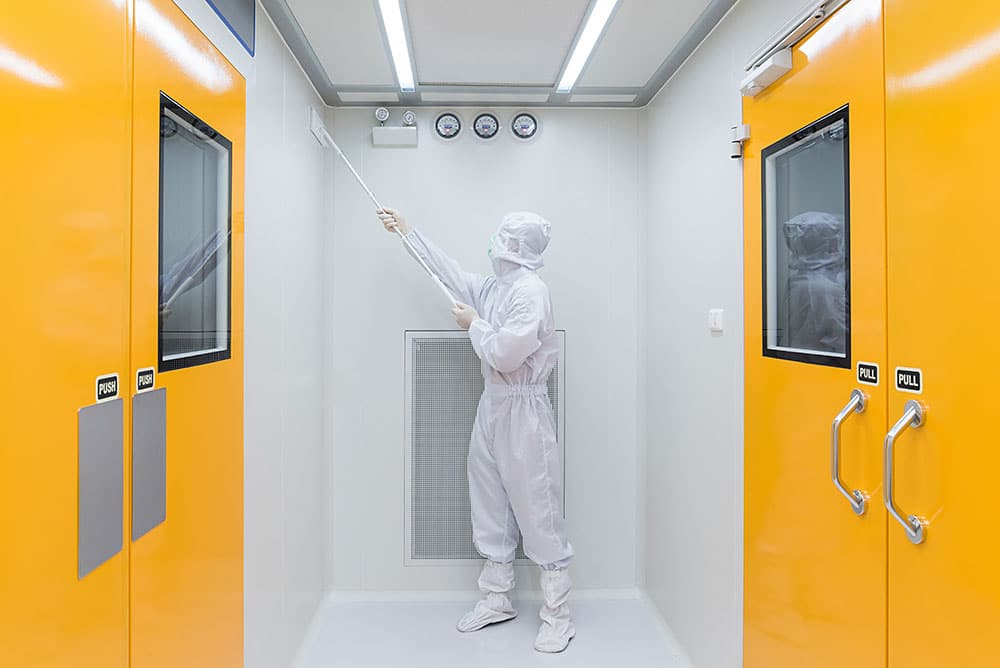 Cleanroom professional wearing full protective apparel using an extension tool to clean and maintain surfaces inside a controlled manufacturing environment