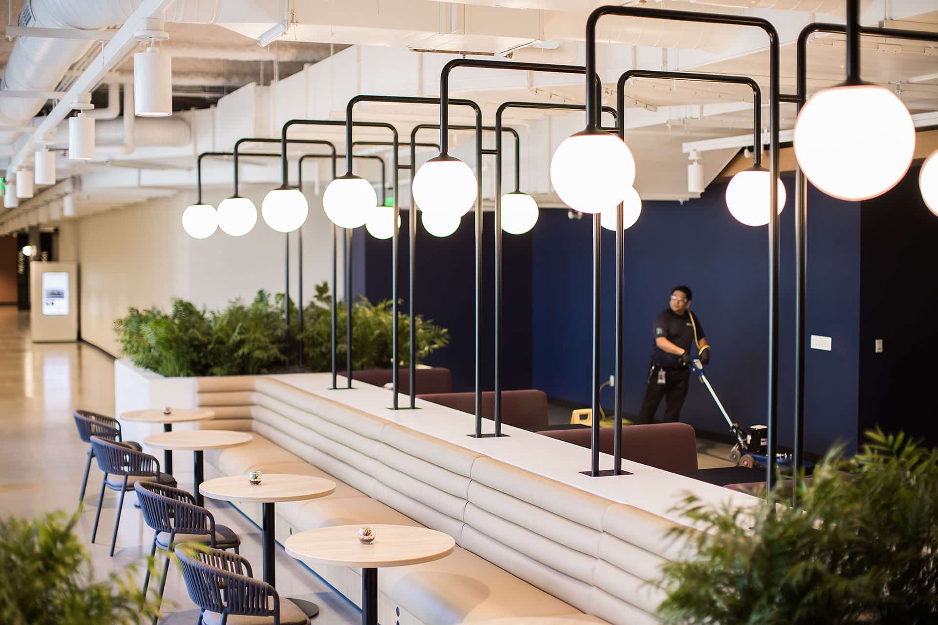 Janitorial professional operating a floor cleaning machine in a modern office lounge and collaboration space