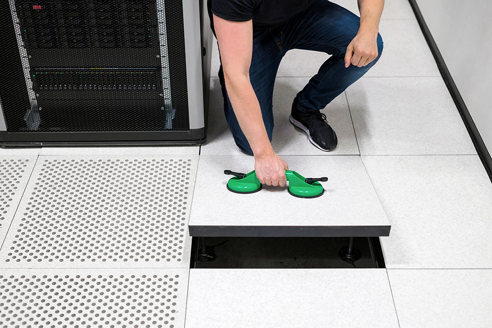 Technician lifting a raised floor panel in a data center to access underfloor infrastructure and equipment