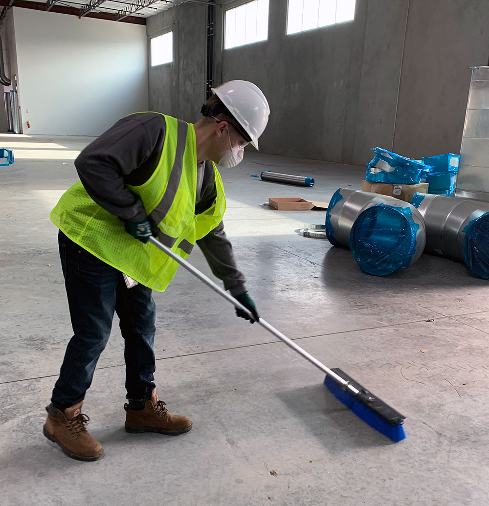 Construction cleaning technician sweeping dust and debris from a newly completed commercial building interior