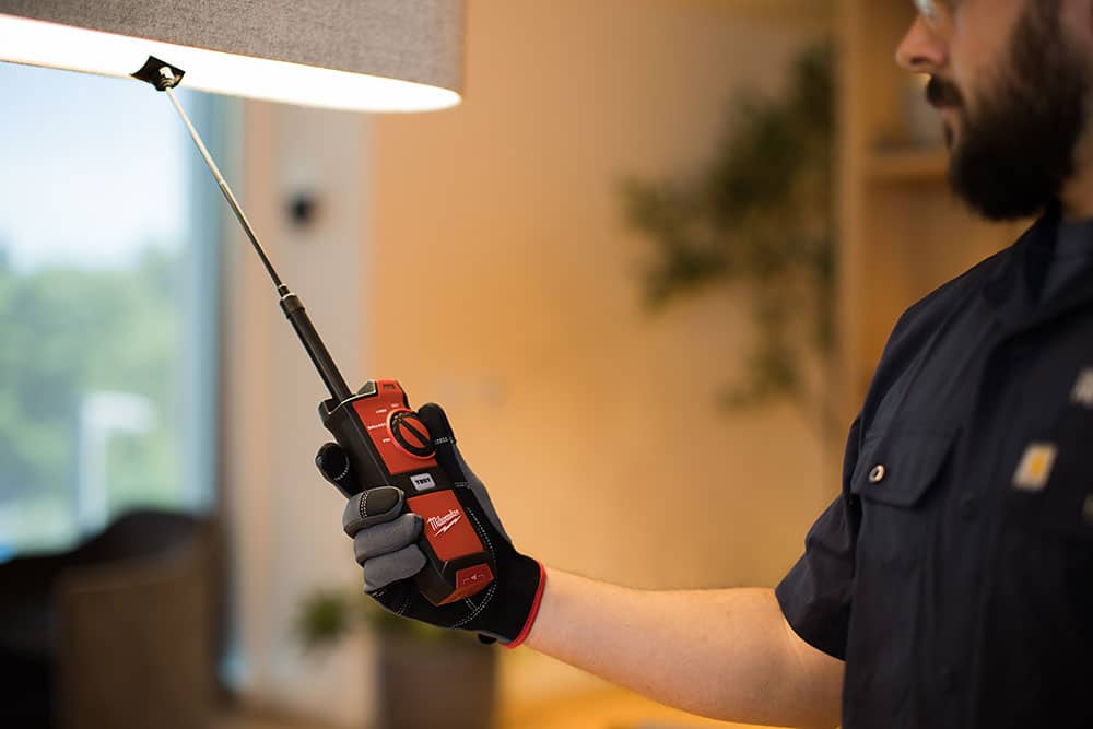 Facility maintenance technician using a handheld inspection device to evaluate building systems in a commercial workplace