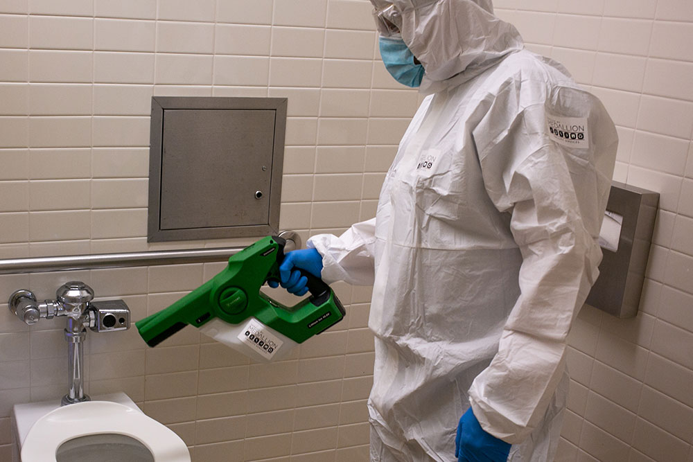 Infection control technician using electrostatic disinfection equipment to sanitize a commercial restroom