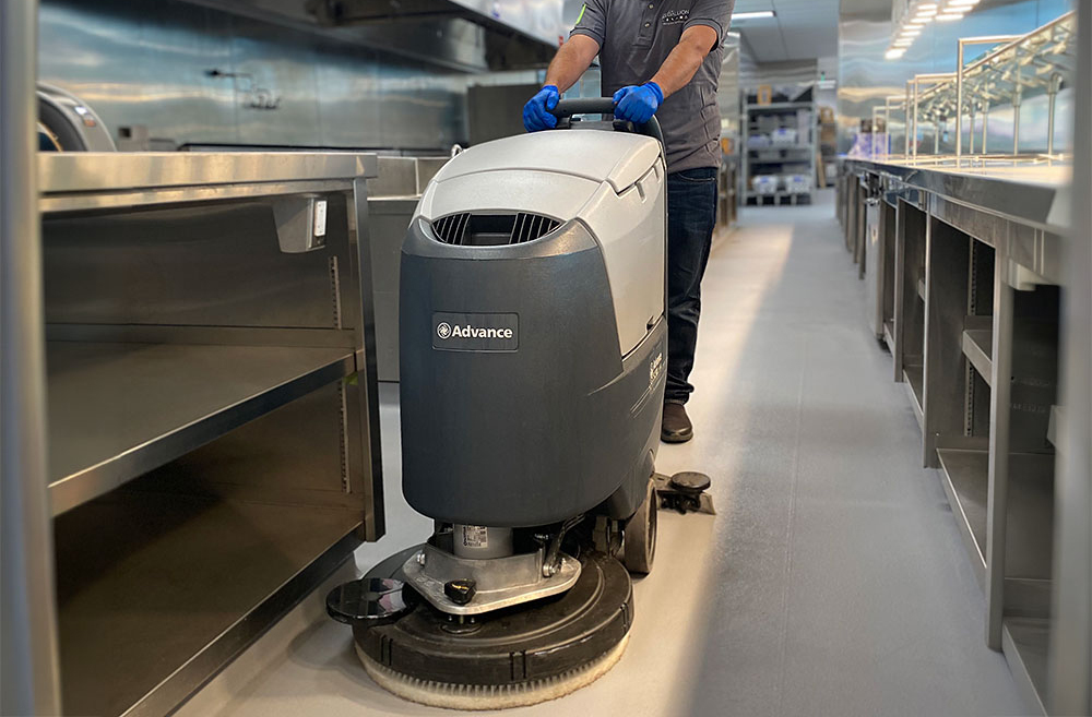 Janitor using a commercial scrubber to clean the floors of a commerical kitchen