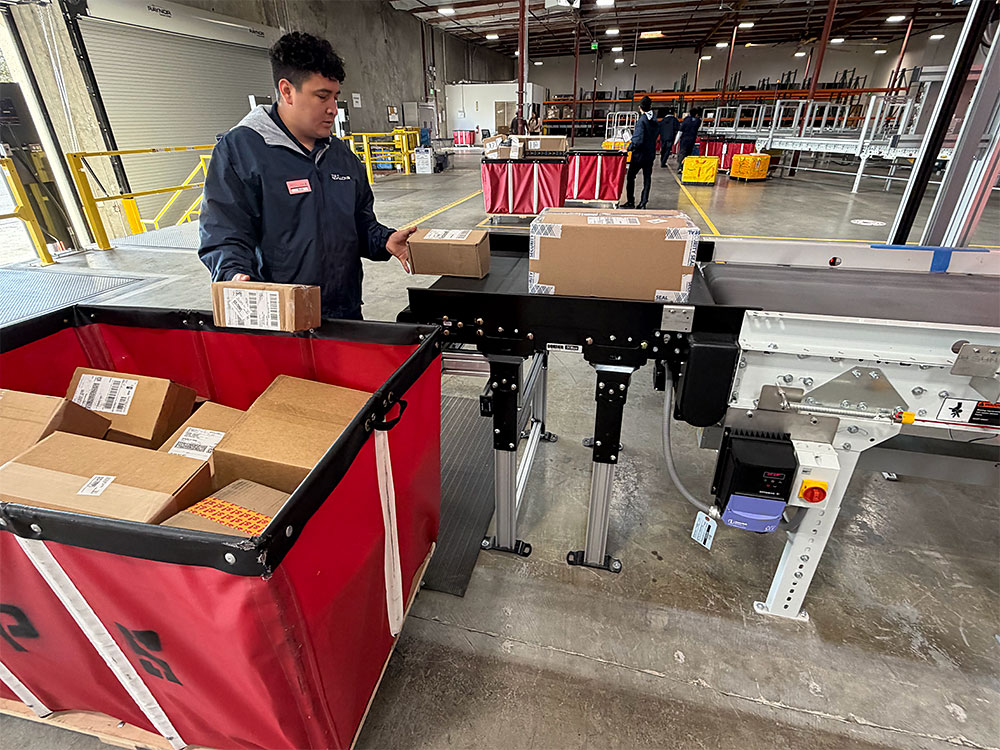 Mailroom clerk sorting packages in onto a conveyer belt in a large mailroom