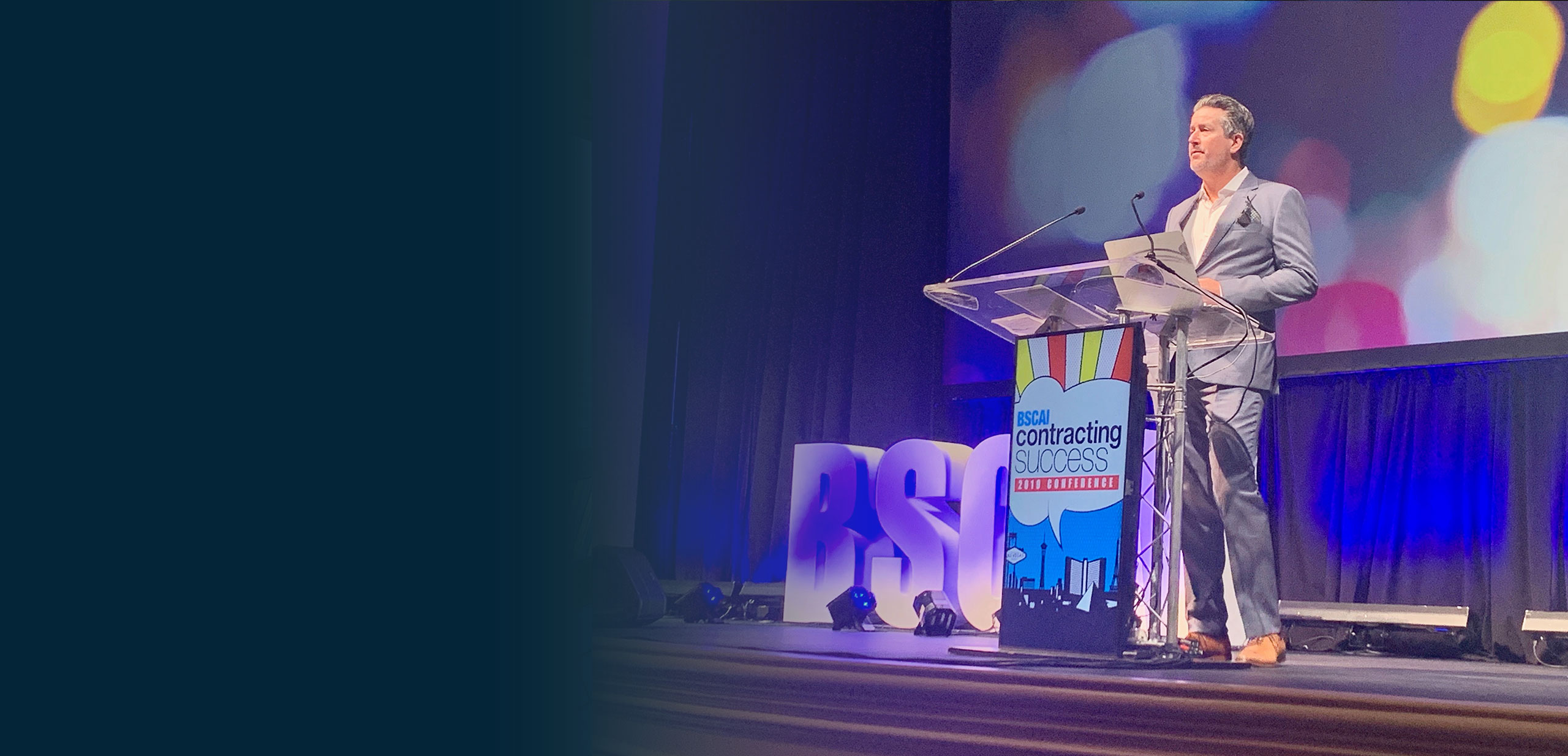 President of Service by Medallion, Roland Strick, speaking on stage in front of a podium 