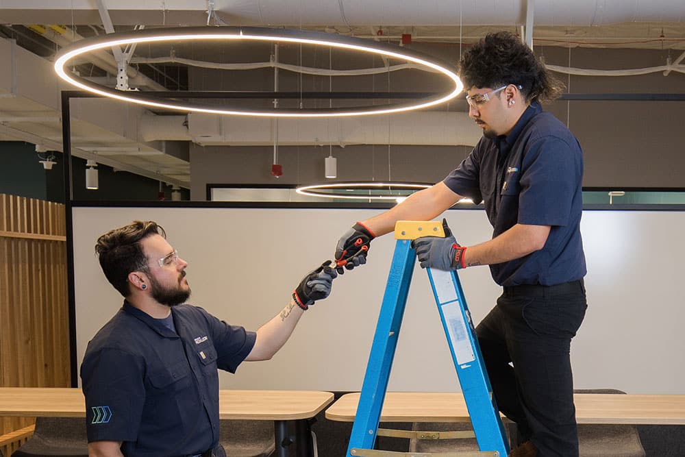 Facility technicians fixing a light and performing building maintenance in a commercial office