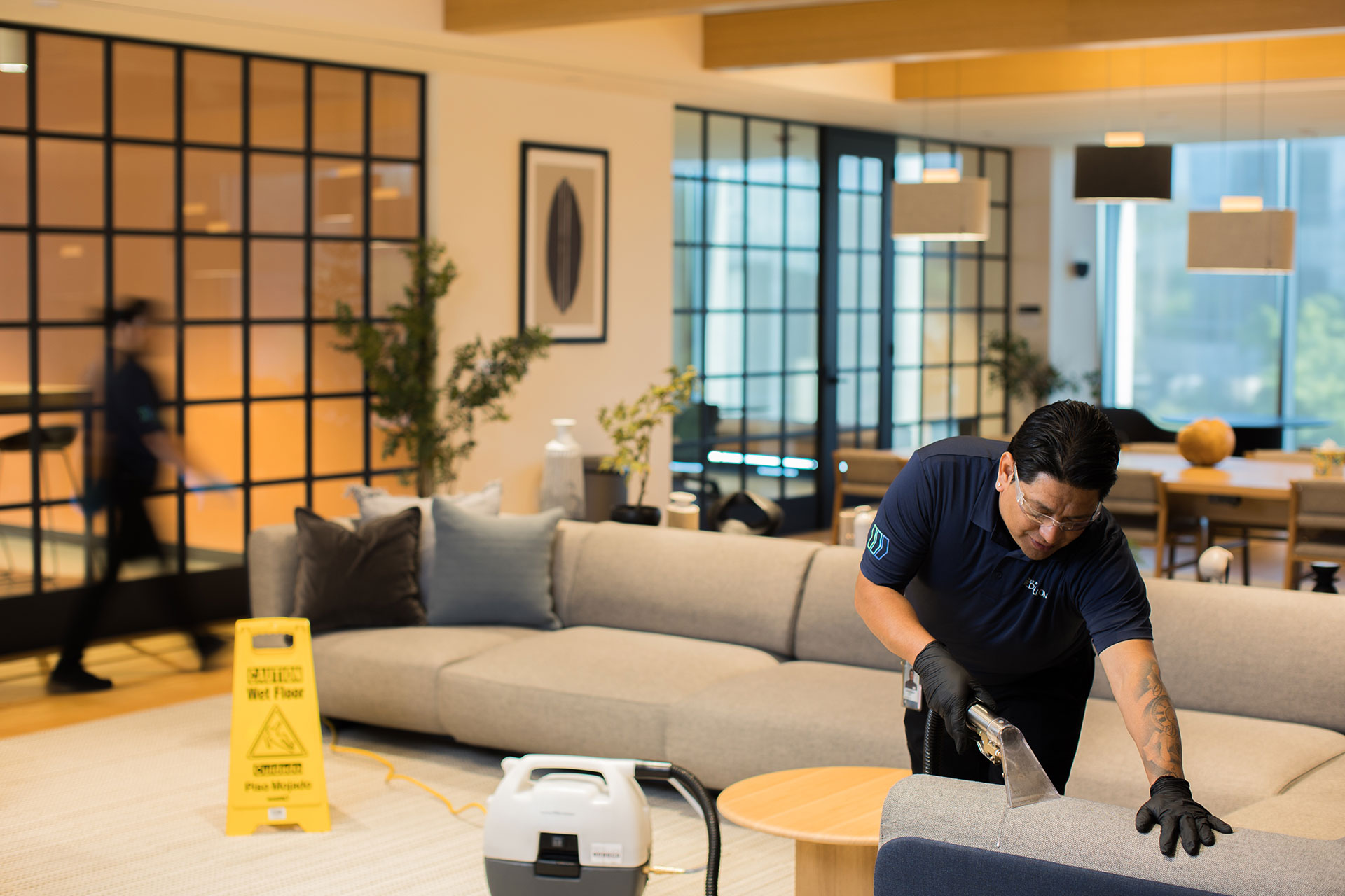 Janitor using a carpet extractor on a couch in a modern office lounge