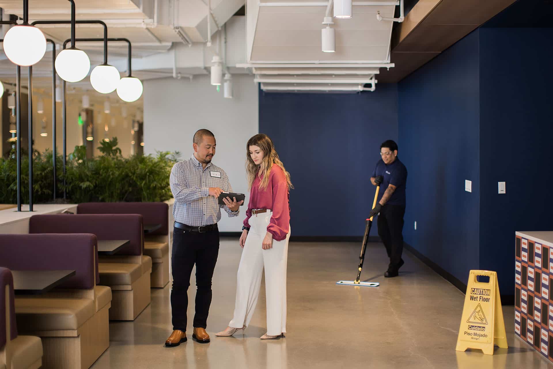 Facility services professional reviewing operational data in the Zen dashboard with a client while janitorial services are performed in the background